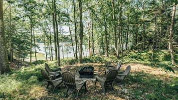 Relax by the fire pit in a serene forest setting, surrounded by Adirondack chairs.