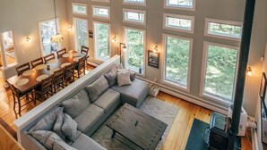 Un loft spacieux avec de hauts plafonds, un grand canapé d’angle, un coin repas et de nombreuses fenêtres offrant une vue sur l’extérieur.