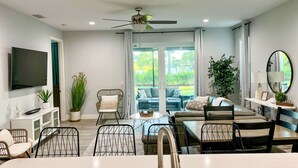 A modern living room with a dining area, a ceiling fan, a flat-screen TV, and a large window with curtains. - Venice Home near Venice Downtown & Venice Beach (Venice)