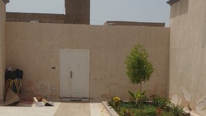 A courtyard with a tiled floor, a small garden with plants, and a white door.