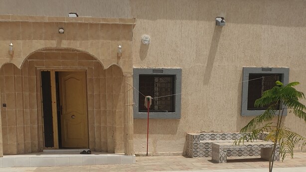 A building with a beige facade, a tiled entrance, and a small tree in the courtyard.