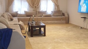 A spacious living room with a beige sofa set, a coffee table, and a flat-screen TV mounted on the wall.