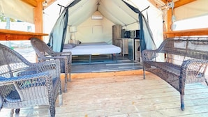 Een tentaccommodatie met een bed, een kleine tafel met een lamp en rieten stoelen.