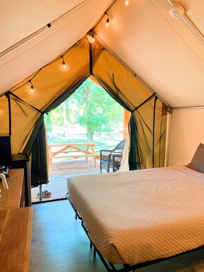 Eine Zelteinrichtung mit Bett, Tisch und Blick auf einen Außenbereich mit Picknicktisch und Stühlen.