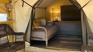 Una tienda de campaña con una cama, una silla y una lámpara.