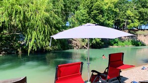 A riverside setting with red and blue folding chairs, a white umbrella, and a rocky riverbank.
