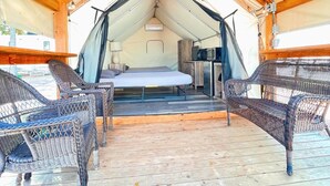 Alojamiento tipo tienda de campaña con una cama, una mesita con lámpara y sillas de mimbre.