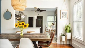 Un coin repas avec une table en bois, des chaises blanches et un vase rempli de tournesols.