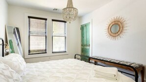 Une chambre à coucher avec un lit, un banc, un lustre et un miroir fixé au mur.