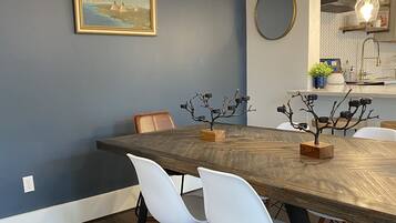 Un coin repas avec une table en bois, des chaises blanches, un luminaire suspendu en rotin et un tableau encadré au mur.
