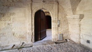 A stone corridor with an arched doorway leading to another room. A small electrical box is mounted on the wall to the right of the doorway.