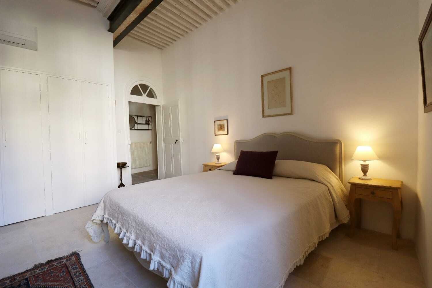 Un dormitorio con una cama grande, dos mesitas de noche con lámparas, una puerta con espejo y un cuadro en la pared.