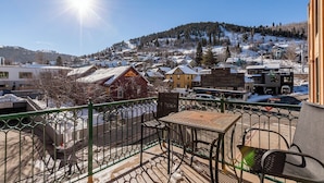 Ein Balkon mit Tisch und Stühlen, mit Blick auf eine verschneite Stadt, Gebäude und einen Berg im Hintergrund.