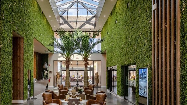 Een ruime lobby met een hoge plafond, groene wanden, en een centrale zithoek met rieten stoelen en een salontafel.
