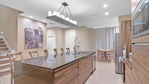 Een moderne keuken met een centraal eiland, roestvrijstalen apparatuur en een eethoek met houten stoelen.