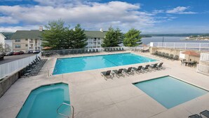 A pool area with two pools, lounge chairs, and a view of a building and water body.