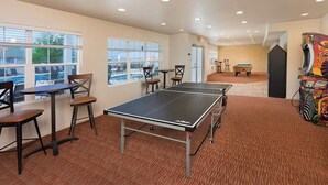 A ping pong table in a room with a pool view, a pool table, and a claw machine.