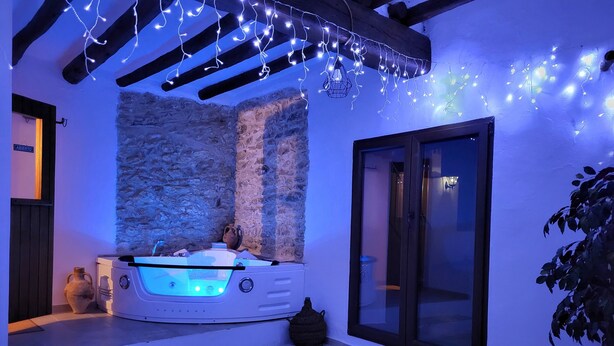 A spa area with a stone wall, a hot tub, and a wooden ceiling. - Rural tourist apartment with spa area. Main Square. PB. Sant Jordi (Sant Jordi)