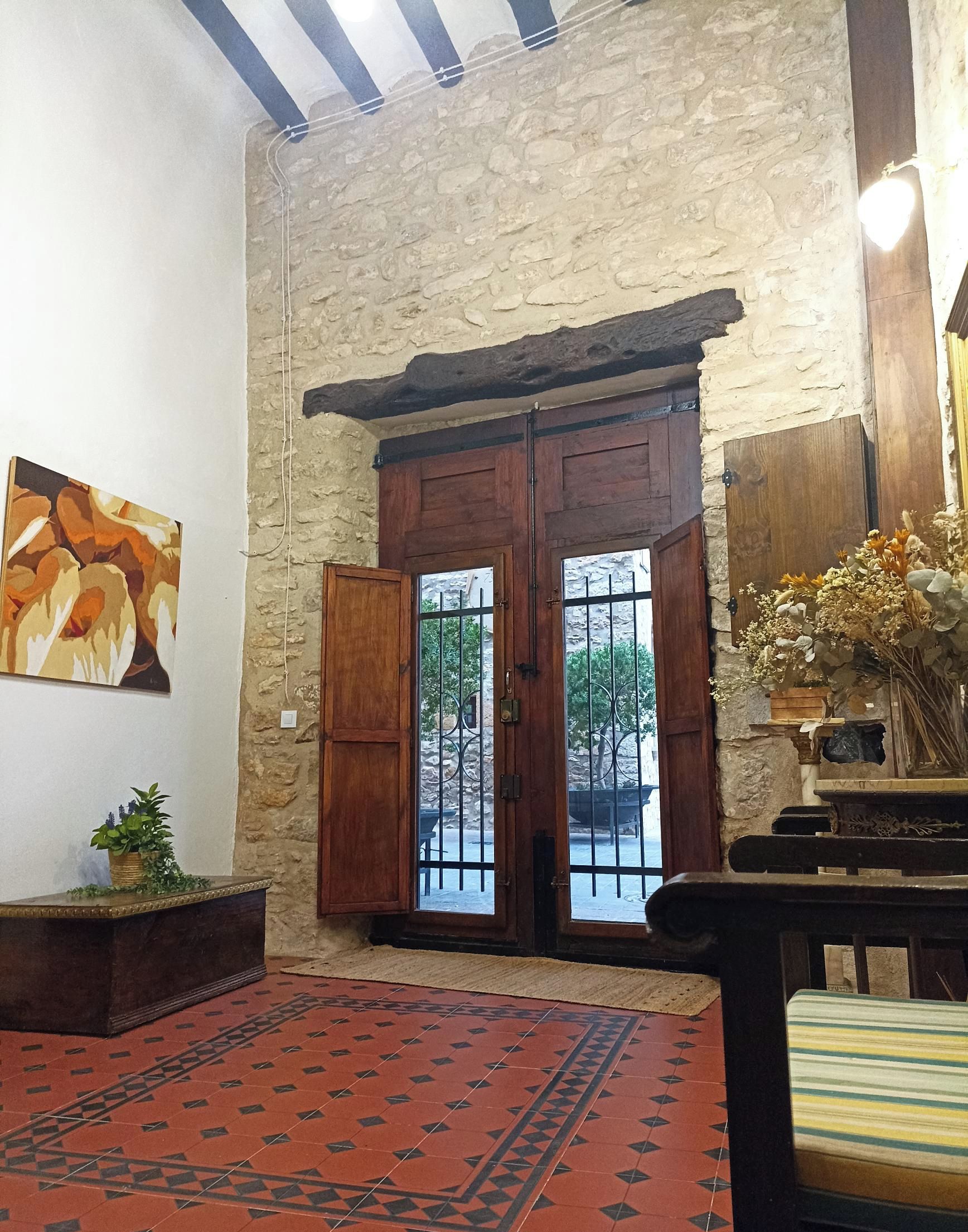 Una habitación con pared de piedra, puertas dobles de madera con barrotes de metal, alfombra roja estampada y un cuadro en la pared.