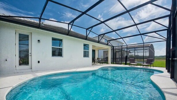 A swimming pool with a covered patio area, a white building with windows, and a clear blue sky.