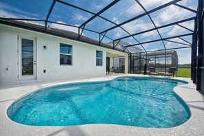 A swimming pool with a covered patio area, a white building with windows, and a clear blue sky. - 4-Bedroom Vacation Home with Pool (Kissimmee)