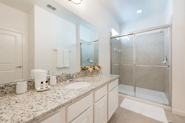 A modern bathroom with a large mirror, two sinks, a shower enclosure, and a granite countertop. - 4-Bedroom Vacation Home with Pool (Kissimmee)