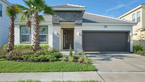 A modern two-story house with a garage, palm trees, and a well-maintained lawn.