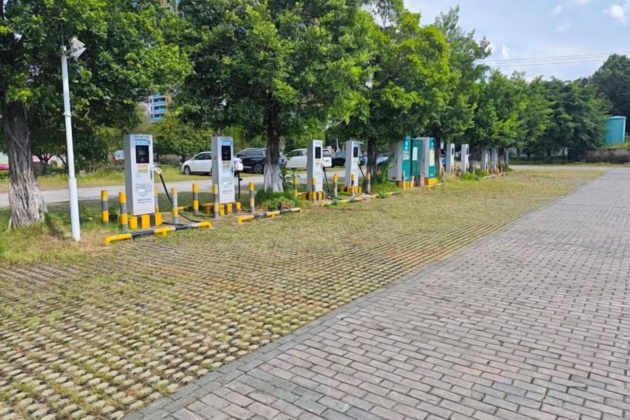 A paved pathway with electric vehicle charging stations and trees in the background.