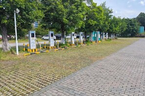 Un chemin pavé, agrémenté de bornes de recharge pour véhicules électriques, avec des arbres en arrière-plan.