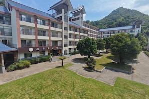Un hôtel à plusieurs étages doté d’une cour intérieure, entouré d’une végétation luxuriante et avec une chaîne de montagnes en toile de fond.