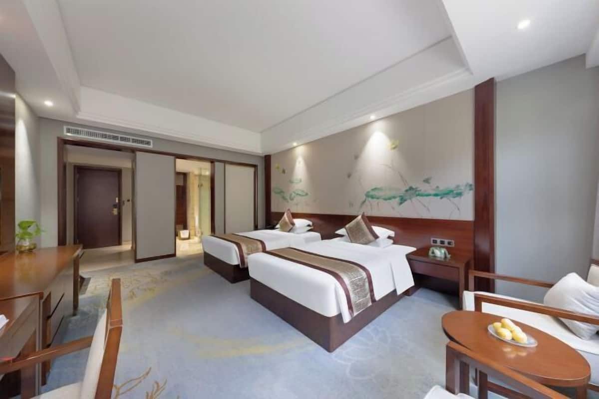 Une chambre d’hôtel avec deux lits, un bureau, une chaise et une petite table sur laquelle se trouve une assiette de fruits.