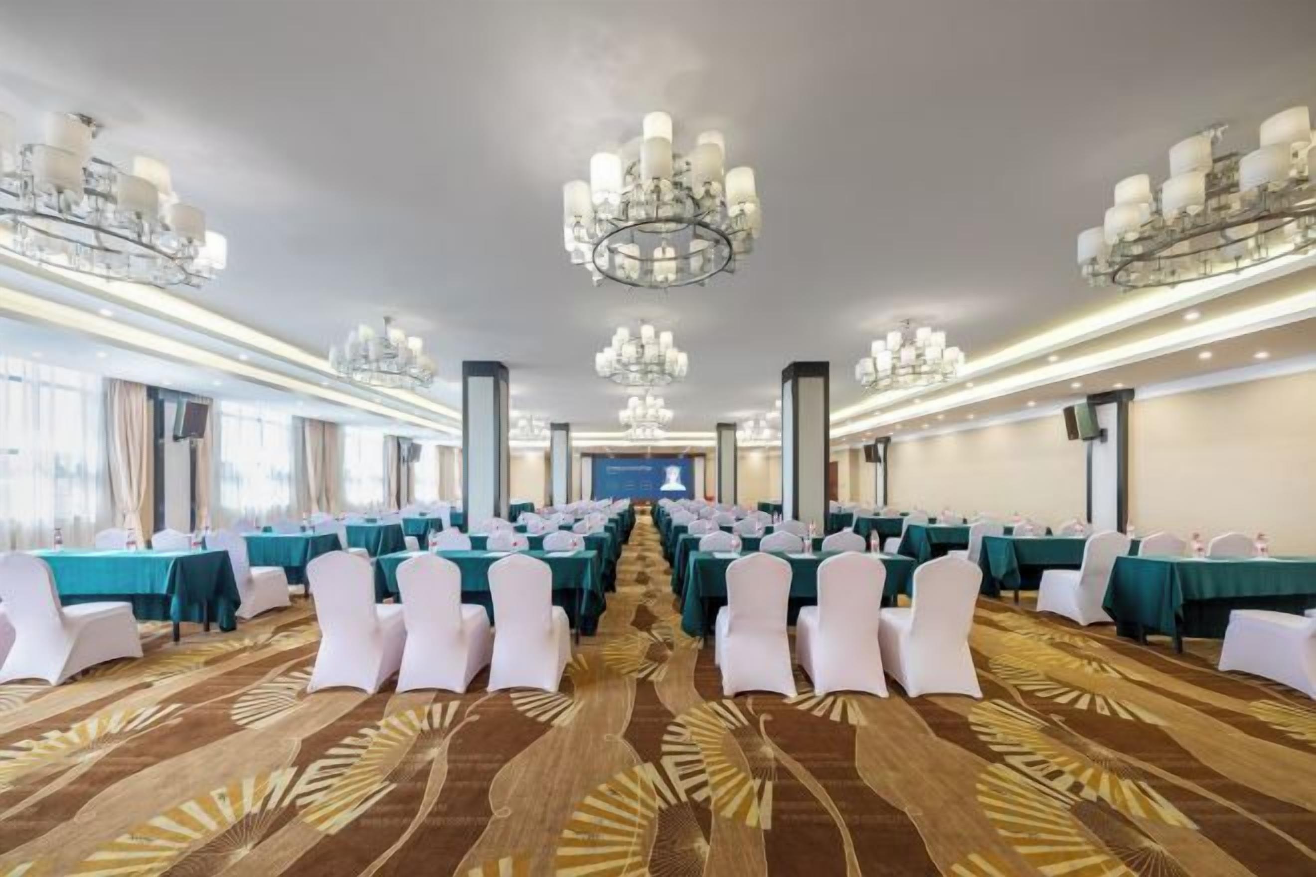 A conference room with rows of tables, white chairs, and chandeliers.