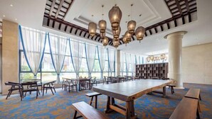 Une pièce spacieuse avec une grande table en bois, plusieurs bancs et un plafond orné de lampes suspendues.