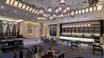 A hotel lobby with multiple dining tables, a reception desk, and a large chandelier.