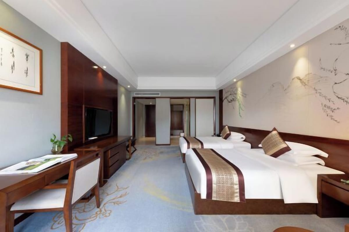 A hotel room with a bed, a desk, a TV, and a wall with artwork.