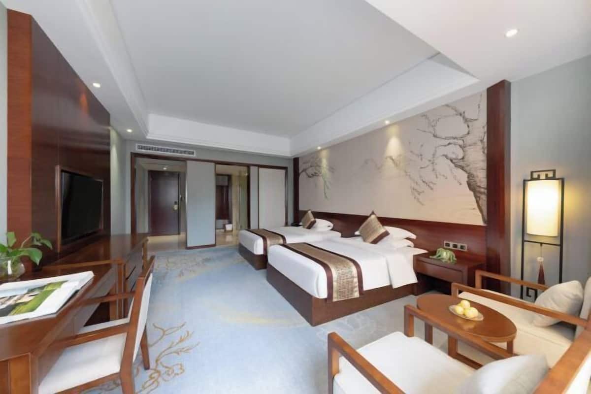 Une chambre d’hôtel avec deux lits, un bureau, une chaise, une petite table et un grand tableau abstrait accroché au mur.