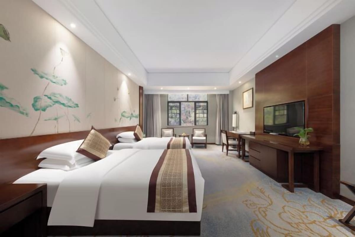 A hotel room with two beds, a desk, a TV, and a large window.