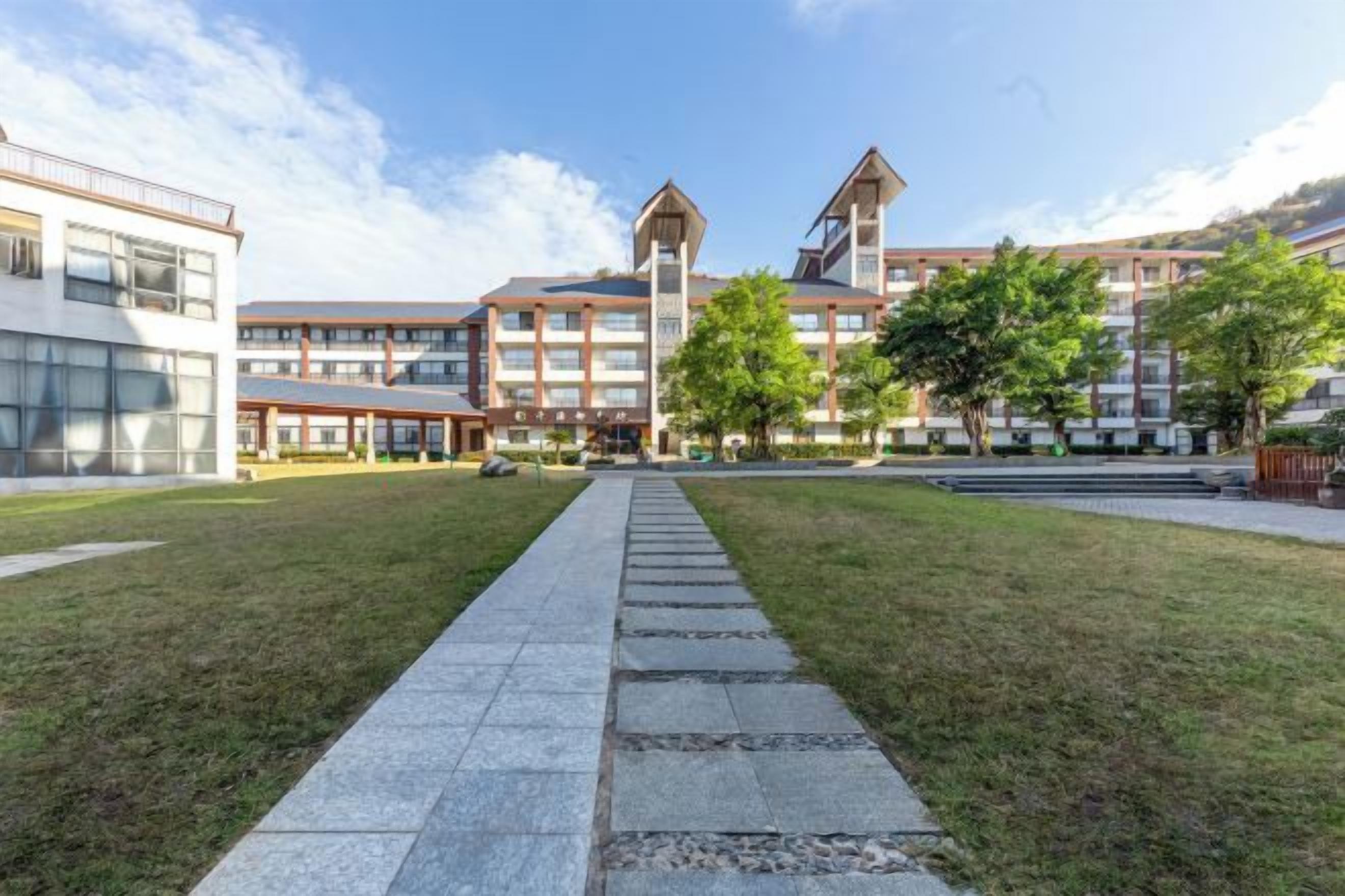 Un patio con un sendero que lleva a un edificio con una torre central y numerosas ventanas.