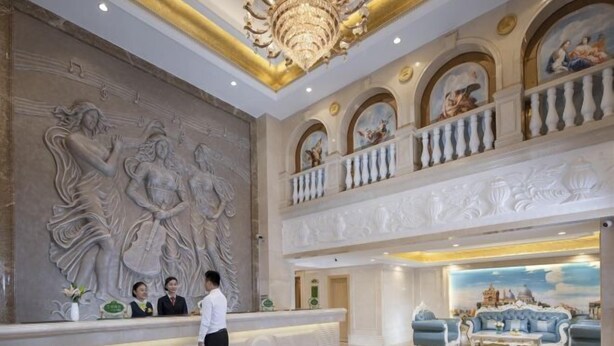 A lobby with a reception desk, a chandelier, and a seating area with a view of a cityscape. - Vienna Hotel (Xinyi Jiaoyucheng River View) (Xinyi)
