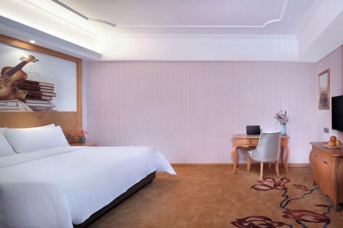 A hotel room with a bed, desk, chair, TV, and a decorative wall piece.