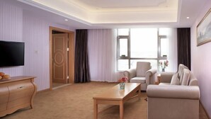 A modern living room with a flat-screen TV, a wooden coffee table, a beige sofa, and a large window with curtains. - Vienna Hotel (Xinyi Jiaoyucheng River View) (Xinyi)