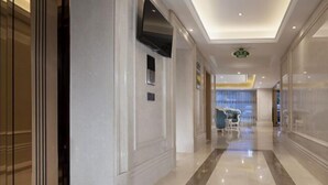 A hotel corridor with a polished marble floor, a flat-screen TV mounted on the wall, and a seating area with chairs and a table in the distance. - Vienna Hotel (Xinyi Jiaoyucheng River View) (Xinyi)