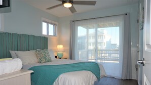 Una camera da letto con un letto, un comodino, una ventola a soffitto, una finestra e un balcone con ringhiera.