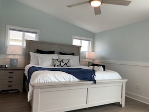 A bedroom with a bed, nightstands, a ceiling fan, and windows.