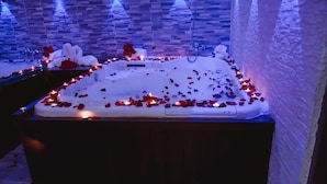 Un baño de spa rodeado de pétalos de rosa y velas, con una pared de piedra y un banco de madera al frente.
