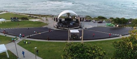 Een openlucht-amfitheater met een podium in het midden, omringd door zitplaatsen, in de buurt van een waterpartij.