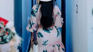 Una mujer con un vestido floral camina por un pasillo con puertas azules y un ventilador de techo.