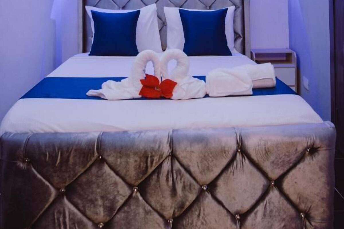 A hotel room with a tufted headboard, a bed with blue and white bedding, a bedside table, an air conditioning unit, and a ceiling fan.