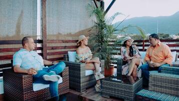 A group of people seated on wicker furniture outdoors with a view of mountains in the background.