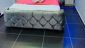 Un dormitorio moderno con un cabecero capitonado, cama con ropa de cama roja y blanca, e iluminación ambiental azul.